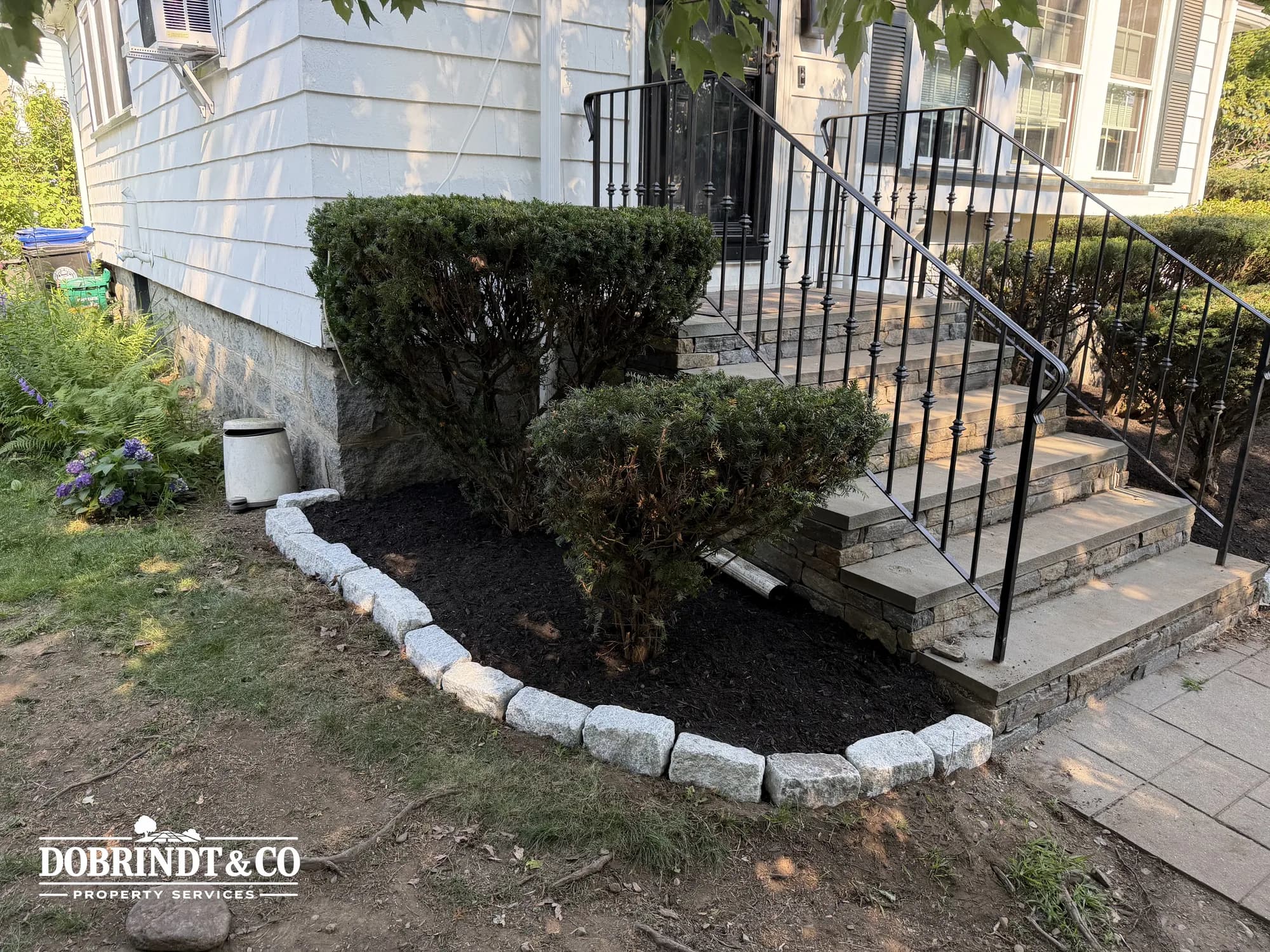Front steps leading to a home's entrance, flanked by neatly trimmed bushes and a landscaped garden with stone borders.