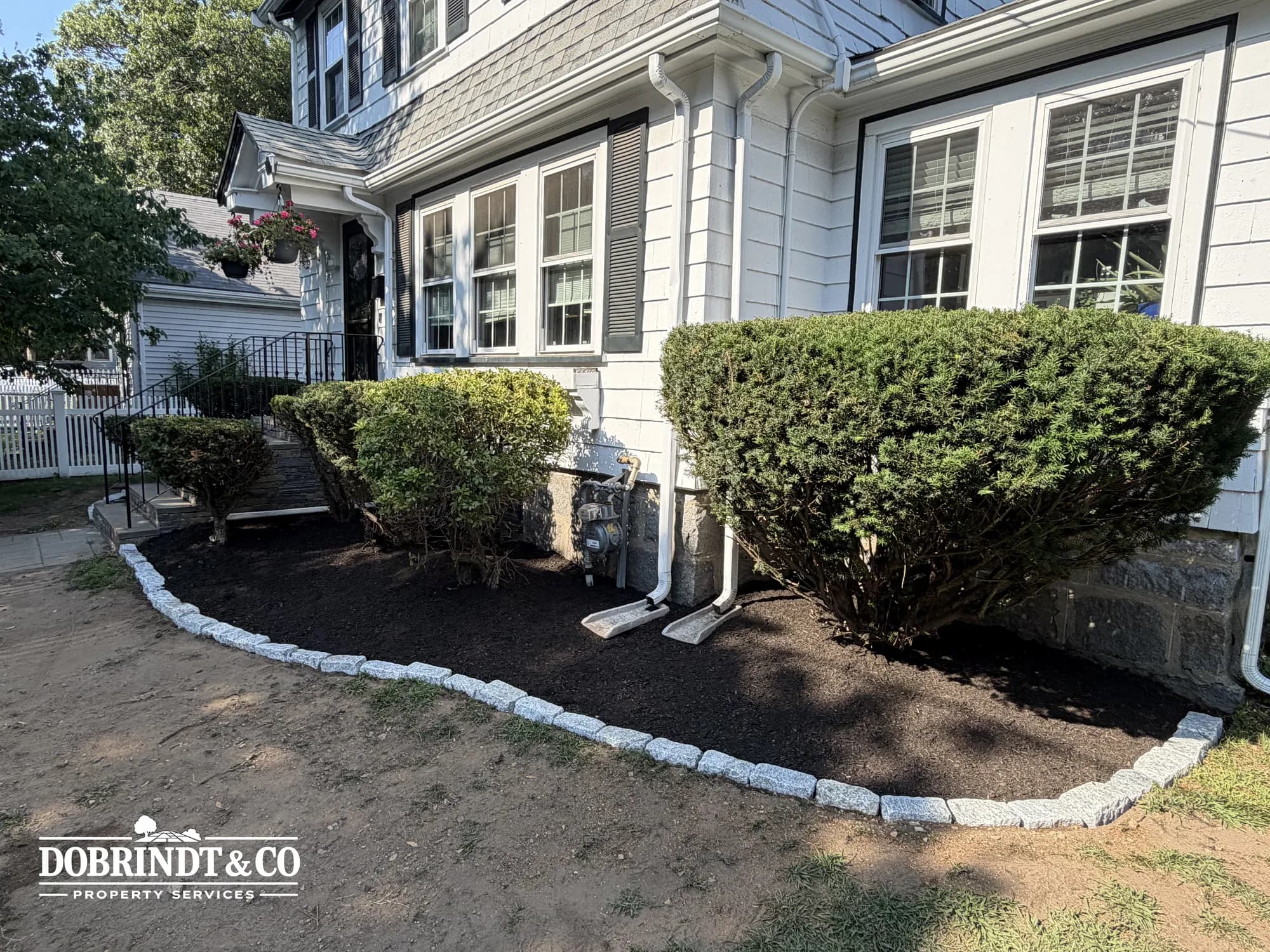 Neatly landscaped front yard with trimmed bushes and freshly laid mulch along a stone border.